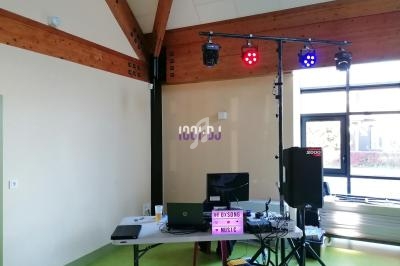 Matériel de DJ installé dans une salle, avec ordinateur, enceintes, projecteurs lumineux et panneau lumineux.