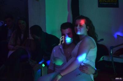 Un couple assis dans une ambiance tamisée avec des lumières colorées, entouré d'autres personnes en arrière-plan.