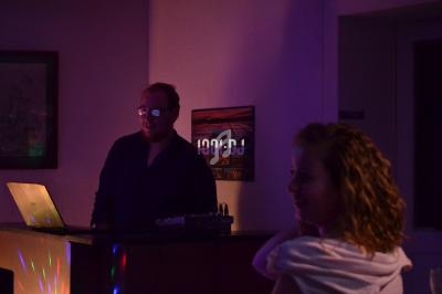 Un DJ mixe de la musique sur un ordinateur portable dans une pièce faiblement éclairée, avec une femme au premier plan.