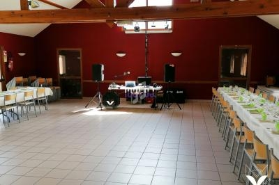 Salle de réception vide avec tables dressées, chaises alignées, et équipement audio installé au fond.