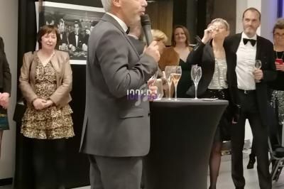 Un homme en costume parle au micro devant un public debout lors d'un événement formel.