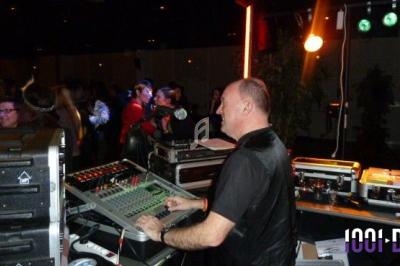 Un DJ mixe de la musique sur une console lors d'une soirée dansante avec des invités en arrière-plan.