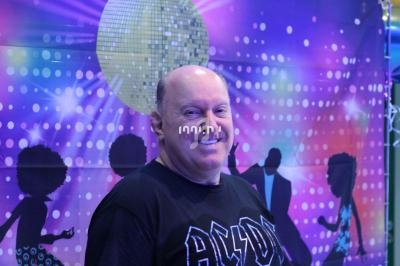 Homme souriant devant un décor coloré avec une boule disco et des silhouettes dansantes en arrière-plan.