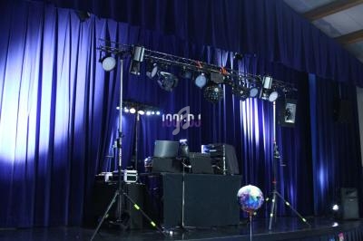 Scène avec rideaux bleus, éclairages de spectacle, équipements audio et une boule disco au premier plan.