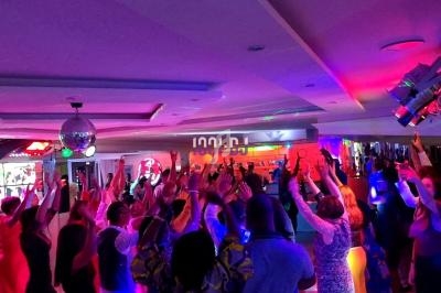 Des personnes dansent sous des lumières colorées dans une salle festive avec une boule disco au plafond.