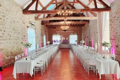 Salle de réception en pierre avec poutres apparentes, tables dressées en longueur et éclairage chaleureux.