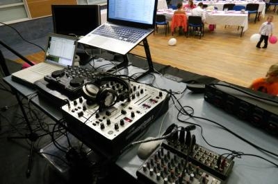 Matériel de DJ avec platines, table de mixage et ordinateurs sur une scène, salle de réception en arrière-plan.