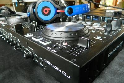 Table de mixage Denon DJ avec des écouteurs posés dessus, entourée d'équipements audio en arrière-plan.