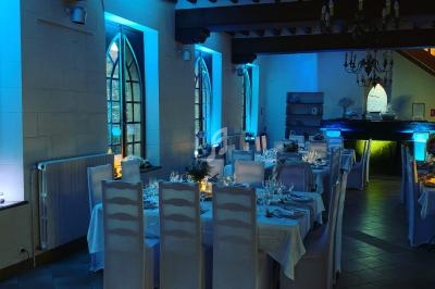 Salle de réception décorée avec des tables dressées, éclairage tamisé bleu et grandes fenêtres en ogive.