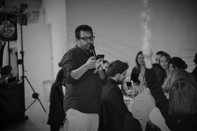 Un homme debout, tenant un micro et un téléphone, s'adresse à un groupe de personnes assises lors d'un événement.