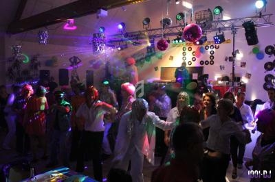 Personnes dansant sous des lumières colorées dans une salle décorée pour une fête avec un DJ en arrière-plan.