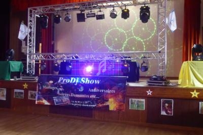 Scène avec une structure lumineuse, projecteurs et une bannière promotionnelle pour des événements festifs.