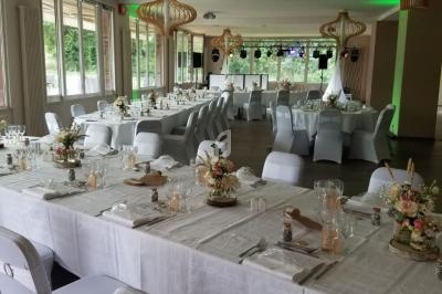Salle de réception décorée avec des tables dressées, nappes blanches et chaises houssées, éclairage naturel et lustres…