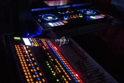 Table de mixage et contrôleur DJ éclairés par des LED colorées, avec un ordinateur portable en arrière-plan.