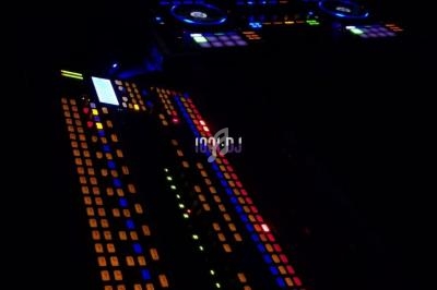 Table de mixage lumineuse avec des boutons colorés, un ordinateur portable affichant des pistes audio en arrière-plan.