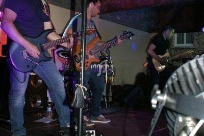 Des musiciens jouent de la guitare électrique sur une scène éclairée dans une salle avec des murs en pierre.