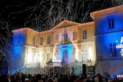 Foule rassemblée devant un bâtiment illuminé, avec des projections lumineuses et des confettis dans l'air.