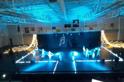 Des danseurs sur une scène éclairée en bleu dans une salle de spectacle, entourés de guirlandes lumineuses.