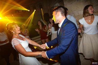 Un couple danse lors d'une fête, entouré d'invités et éclairé par des lumières colorées.