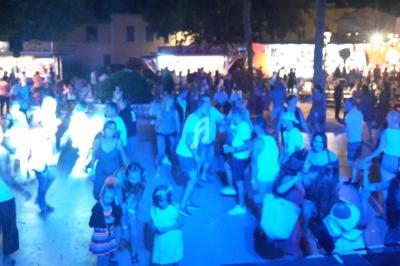 Foule dansante en extérieur sous des lumières bleues, avec des stands éclairés en arrière-plan.