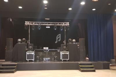 Scène équipée de matériel de sonorisation et d'éclairage, entourée de rideaux bleus dans une salle de spectacle.