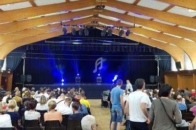 Salle comble avec des spectateurs assis face à une scène éclairée par des projecteurs bleus.