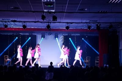 Des danseuses en tenue rose et blanche exécutent une chorégraphie sur une scène éclairée par des projecteurs.