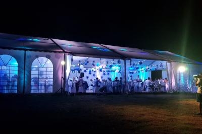 Grande tente éclairée en bleu et blanc, abritant un événement nocturne avec des invités assis à des tables.