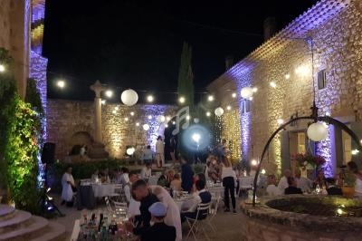 Cour extérieure éclairée avec des guirlandes lumineuses, tables dressées et invités réunis pour une réception en soirée.