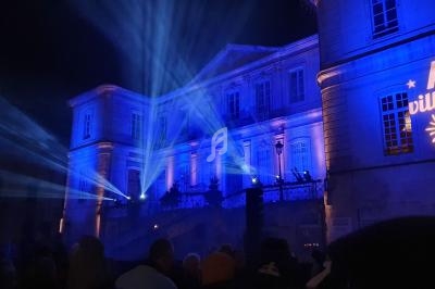Façade d'un bâtiment illuminé en bleu avec des projections lumineuses et une foule rassemblée au premier plan.