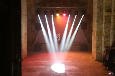 Projecteurs lumineux colorés éclairant une scène vide dans un espace en pierre avec des enceintes sur les côtés.