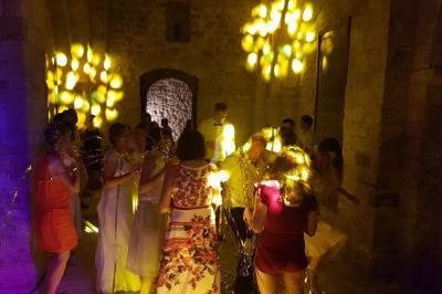 Des personnes dansent et discutent dans une salle en pierre éclairée par des lumières jaunes et violettes.