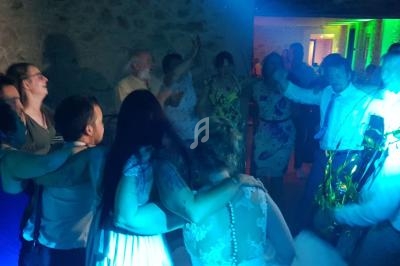 Groupe de personnes dansant et s'amusant lors d'une fête, éclairées par des lumières colorées dans une salle en pierre.