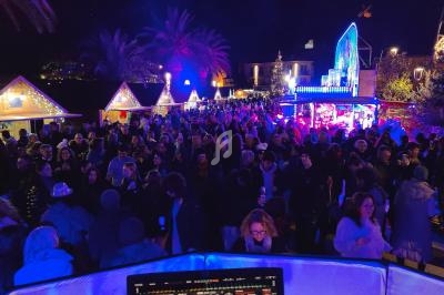 Foule rassemblée de nuit dans un marché illuminé avec des chalets décorés et des lumières colorées.