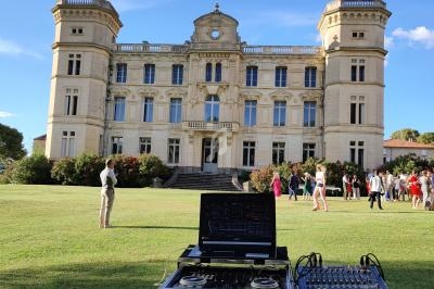 Console de DJ en premier plan avec un château en arrière-plan et des invités sur une pelouse lors d'un événement.