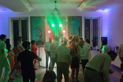 Des personnes dansent dans une salle éclairée par des lumières colorées, avec un lustre et des décorations murales.