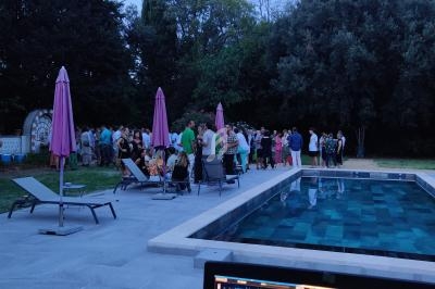 Groupe de personnes rassemblées près d'une piscine en soirée, avec des transats et des parasols autour.