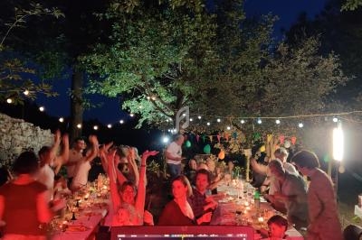 Des convives dînent et dansent en extérieur sous des guirlandes lumineuses, avec une table festive et un écran de DJ au…