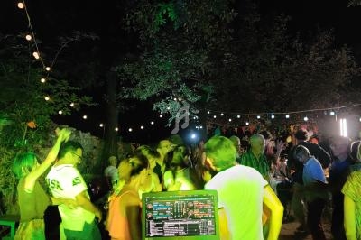 Des personnes dansent en plein air la nuit sous des guirlandes lumineuses, avec une table de mixage au premier plan.