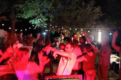 Groupe de personnes dansant en extérieur la nuit, éclairé par des guirlandes lumineuses et des lumières colorées.