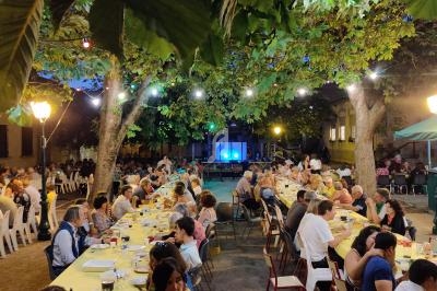 Des personnes dînent à de longues tables sous des arbres illuminés par des guirlandes lumineuses dans une ambiance festive.