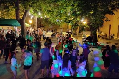 Vue depuis une table de mixage sur une fête en plein air avec des personnes dansant sous des guirlandes lumineuses.