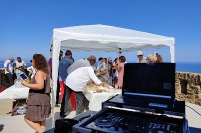 Un groupe de personnes partage un repas sous une tente blanche en extérieur, avec une table de mixage au premier plan.