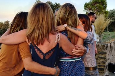 Un groupe de personnes s'enlaçant chaleureusement en extérieur, près d'un paysage naturel au coucher du soleil.