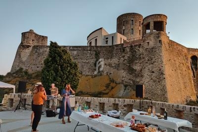Personnes discutant près de tables dressées pour un événement en plein air devant un château historique au coucher du soleil.