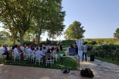 Cérémonie en plein air avec des invités assis, un officiant et un couple devant une arche décorée, entourés de verdure.