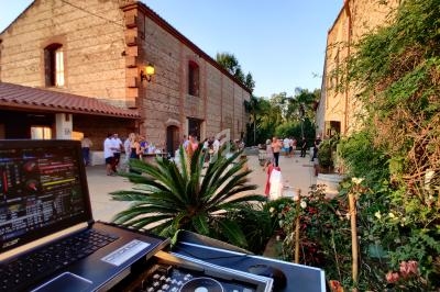 Vue d'une cour extérieure avec des invités rassemblés, un ordinateur et une table de mixage au premier plan.