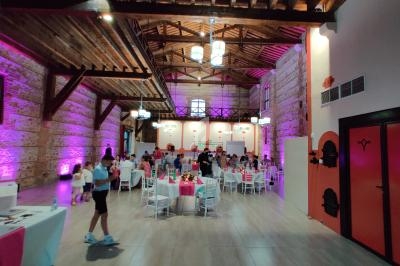 Salle en pierre avec plafond en bois, décorée pour un événement, tables dressées et invités discutant.