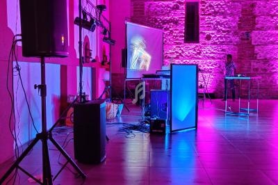 Salle éclairée de lumières roses avec un équipement audio, un écran de projection et une personne à une table.