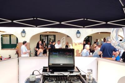 Poste de DJ sous une tente, avec une table de mixage et un ordinateur, face à des invités lors d'un événement en extérieur.